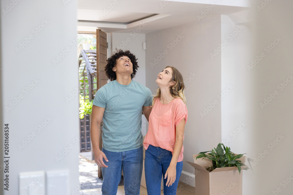 Obraz premium Couple standing together in hallway at open wooden front door unpacking box with potted plant