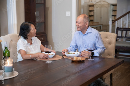 Fotografie Asian couple sitting at dark wooden dining table sharing meal, holding bowls and