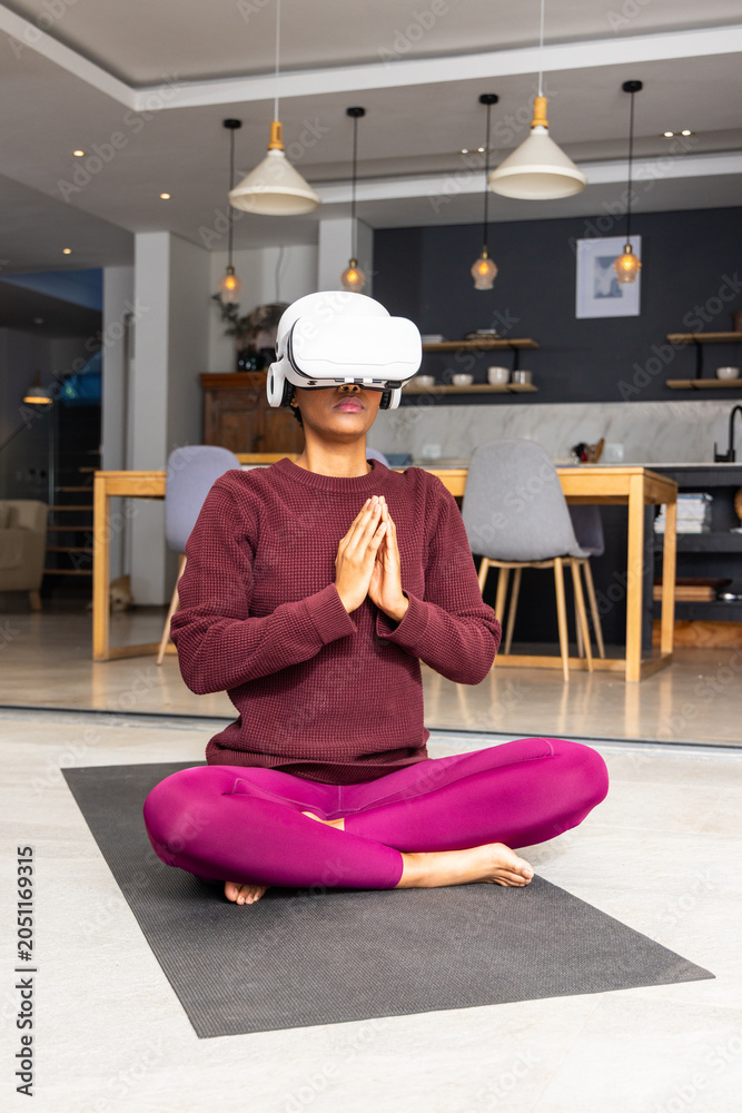 Naklejka premium Person is meditating while wearing white VR headset on black yoga mat in open-plan kitchen