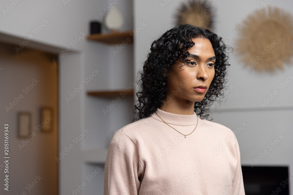 Obraz premium Non-binary person standing in living room wearing pale pink sweater, gold necklace, sunburst decor