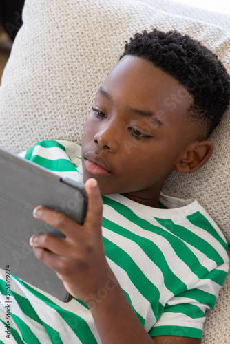 African American preteen reclining on cushion at home in green T-shirt holding tablet in dark-case