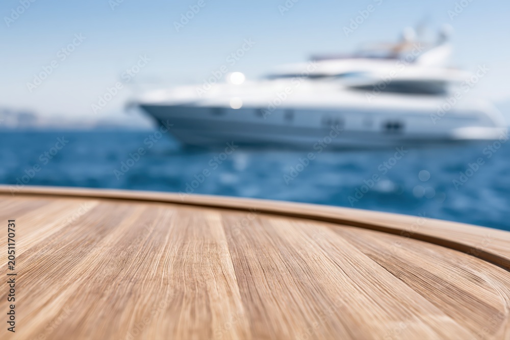 Fototapeta premium Close-up of a wooden deck in the foreground with a luxury yacht sailing on the blue ocean in the background.