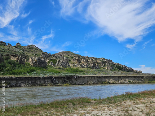 Natural landscape of a river flowing past hills on the opposite riverbank and a blue sky with white clouds.