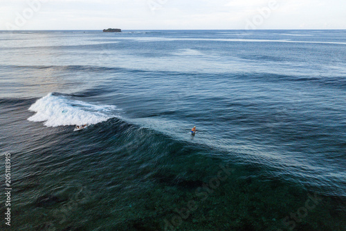 Aerial view of surfers riding a breaking wave in the clear blue ocean near Siargao Island General Luna, Caraga, Philippines.