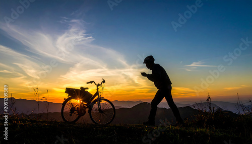 Silhouette of a person standing next to a bicycle against a vibrant sunset sky, capturing the serene beauty of the outdoors.