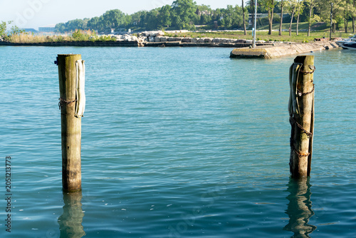 Obraz na płótnie Two weathered wooden posts emerge from calm blue water, draped with ropes used f