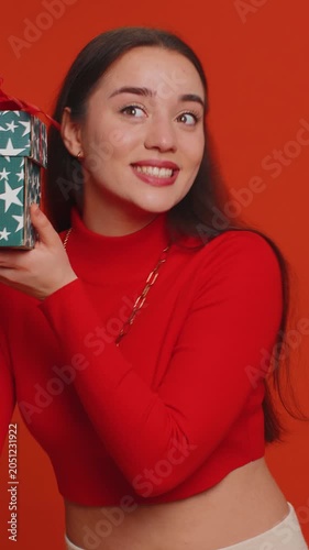 Happy pretty woman opening gift box, unwrapping birthday surprise and expressing great happiness amazement, satisfied with best present bonus. Young lovely girl isolated on red studio background