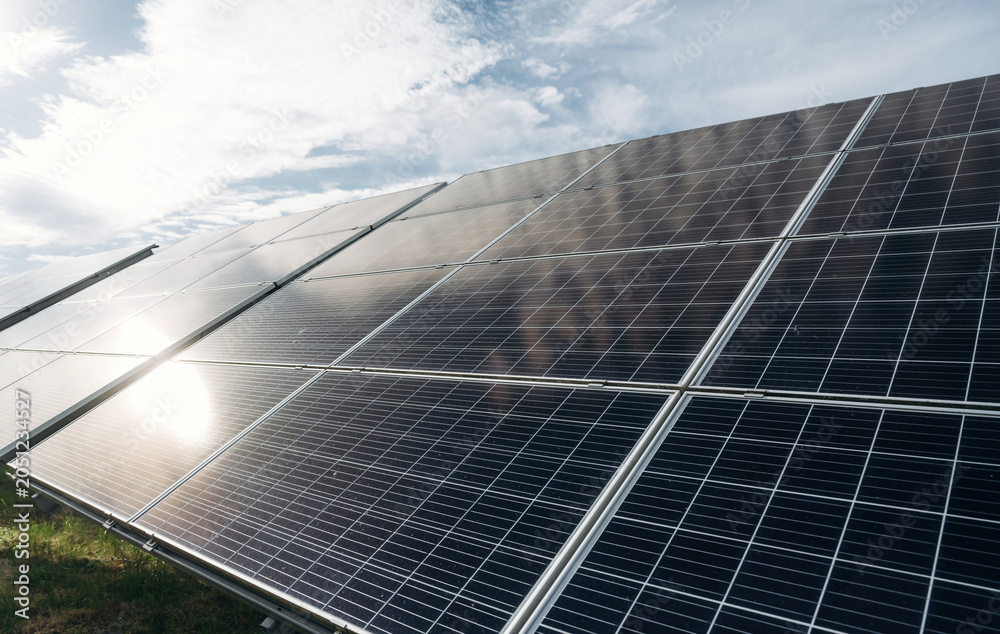 Naklejka premium Solar panels installed in a green field under a bright sky, showcasing renewable energy technology with reflections on the glass surface and grass in the foreground
