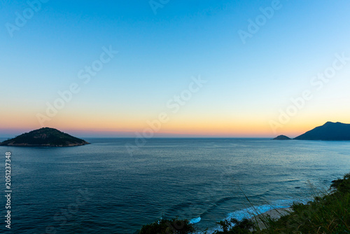 Paisagem marinha tropical com horizonte amplo, ilhas distantes e céu iluminado pelo pôr do sol, Praia de Grumari, Rio de Janeiro