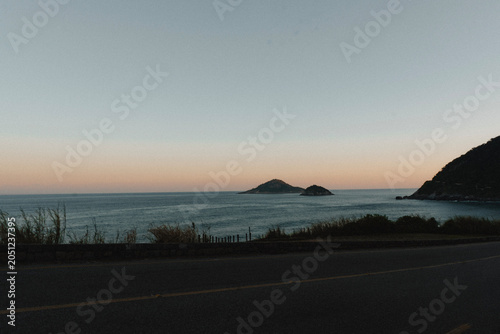 Paisagem costeira com mar calmo, ilhas no horizonte e céu colorido ao entardecer, Praia de Grumari, Rio de Janeiro