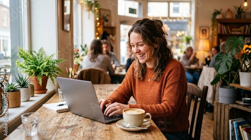 Woman happily working on laptop in a cozy cafe with plants and coffee
