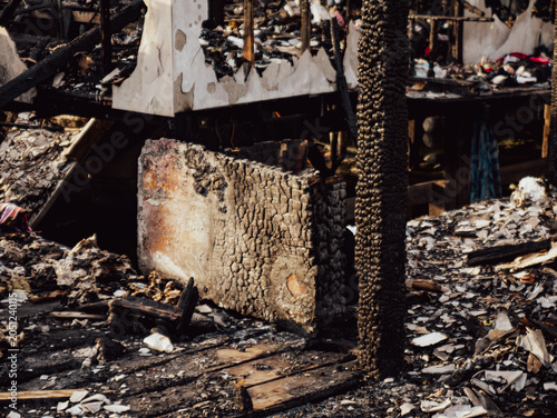 Fire disaster aftermath scene showing burned destroyed house interior with charred wood debris ash and collapsed furniture in residential fire