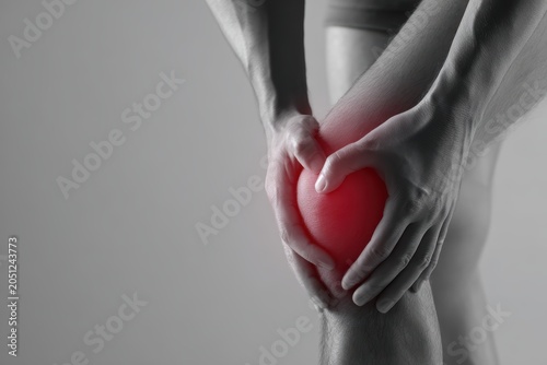 Knee Pain Sensation: A close-up shot highlighting a person's hands clutching a knee, with a vibrant red glow emphasizing the area of discomfort and pain, symbolizing physical ailment and suffering.