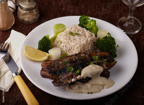 Grilled herring fillets with rice and vegetables and garnished with fish sauce.