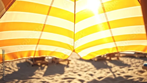 Low angle shot of translucent amber striped umbrella with warm sunbeam lens flare on sand