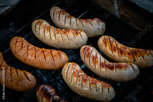 Grilling sausages on barbecue grill during an outdoor gathering or summer cookout.
