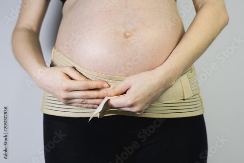 Woman putting on a supportive maternity belly band for back relief and comfort during pregnancy.