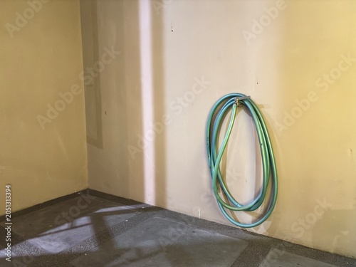 Green rubber watering hose stored on a cream wall above a stone floor, ready for gardening and backyard chores.