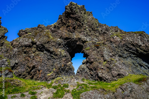 Fotografía Natural rock arch formation with green moss and blue sky background,ICELAND
