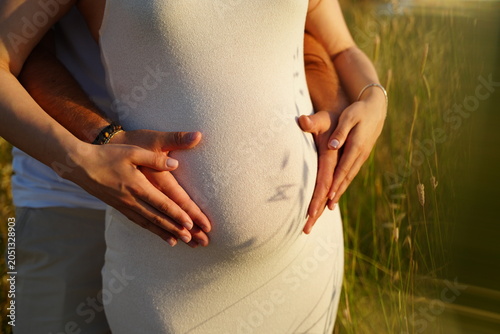 Obraz na plátně Close view of expectant parents gently holding pregnant belly in golden sunset light