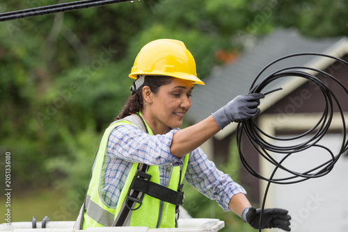 Hispanic female cable lineman stringing a new line in the rain