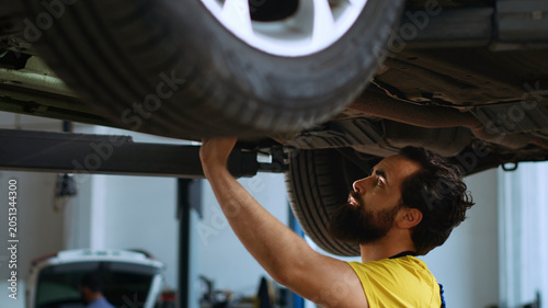 Foto Certified repairman underneath vehicle on overhead lift in garage, checking parts