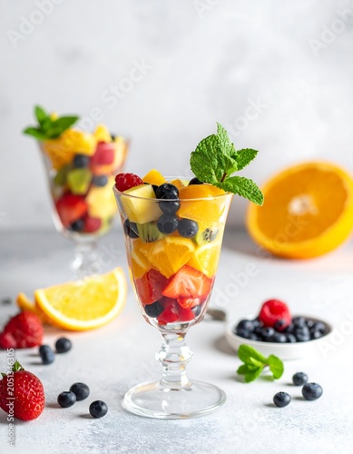 A colorful arrangement of fresh fruit and mint in elegant glasses on a light surface