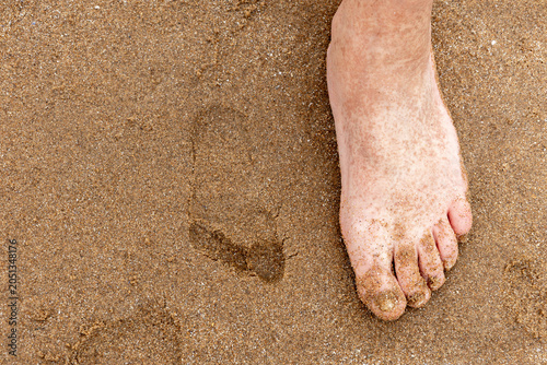 Close-up of a bare foot stepping into soft sand with a visible footprint, showing summer travel and outdoor relaxation