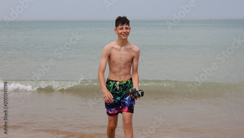 Teenage boy walking on beach and holding big piece of stone.Young boy playing on a sandy beach by the calm sea under a cloudy sky
