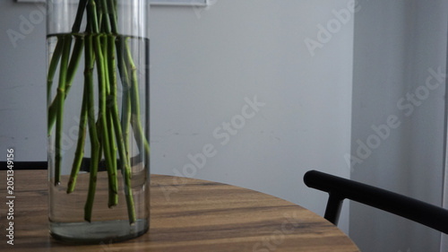 Canvas-taulu Green flower stems in a glass cylinder vase filled with water standing on a wooden dining table