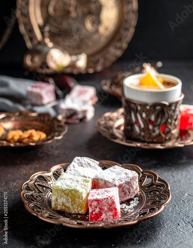 A colorful arrangement of traditional sweets on ornate metal plates with a cup of tea