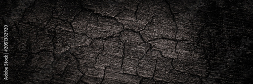 Texture of cracked dark surface with deep lines showing wear and age in a close-up view during daylight