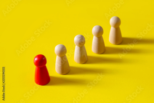 Leadership and unique person concept; The red stand out in front of row of wooden figures 