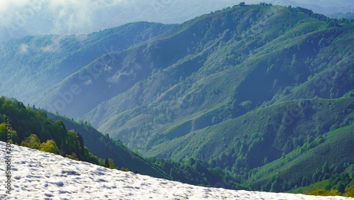 Foto Majestic layers of lush green mountain ridges partially covered in lingering snow