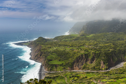 Impresionante vista aérea de los acantilados verdes, el litoral de Fajazinha y las olas del océano Atlántico bajo nubes bajas en la isla de Flores.