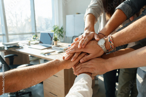 Team of diverse coworkers stacking hands in modern office for teamwork and collaboration