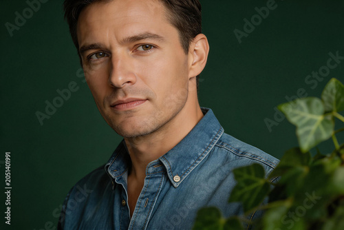 Portrait of a serious young man wearing a denim shirt with green plant in foreground