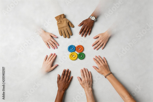 Diverse Group of Hands Surrounding Colorful Interlocking Gears Symbolizing Teamwork and Collaboration