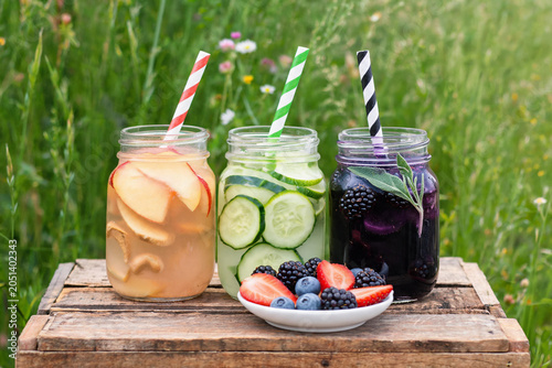 Three jars of infused water with fruit and herb garnishes on rustic wooden crate outdoors