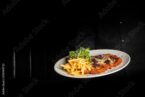 Foto A waiter holding a plate of chicken parmigiana served with french fries and a fr