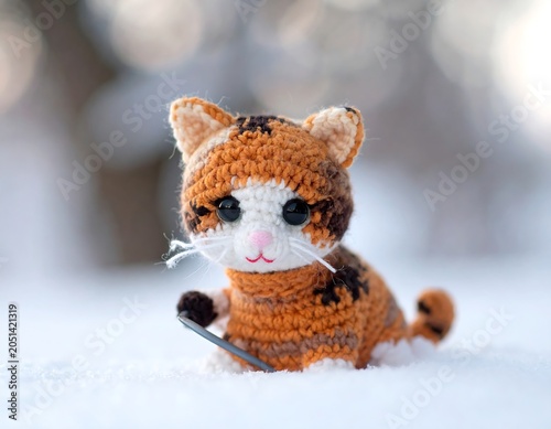 A crocheted orange, black, and white cat toy with whiskers sitting in snow