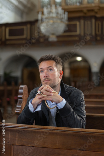 Serene Catholic man praying with a rosary in his hands, at the church. Concept of a deep faith, devotion, and spiritual strength.