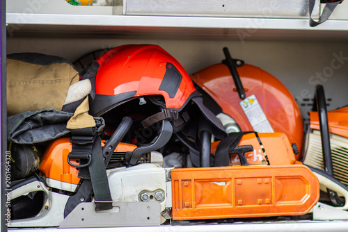 Safety equipment including orange helmet, gloves, and chainsaw stored in a toolbox, showcasing essential tools for outdoor work and maintenance tasks