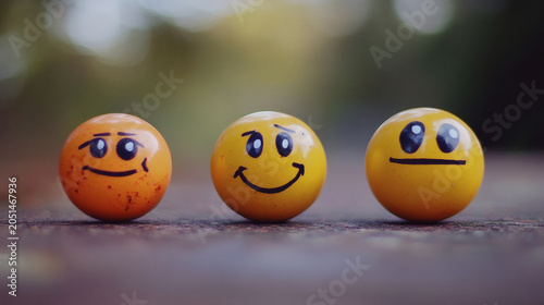 Three yellow balls with different drawn emotions and smiley faces standing in a row