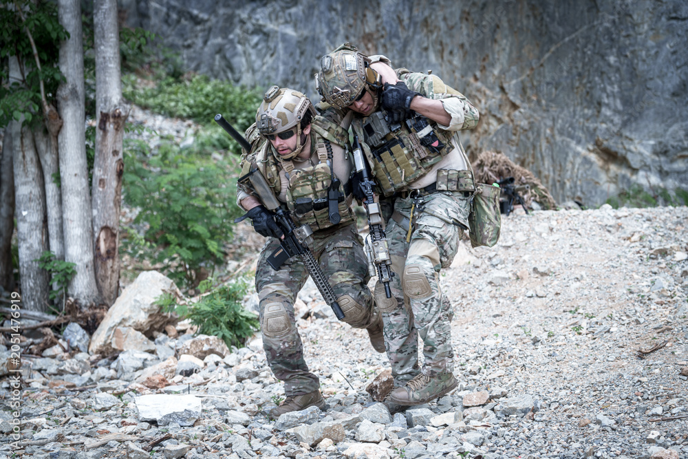 Fototapeta premium Soldiers assisting injured comrade during tactical training exercise in rocky terrain