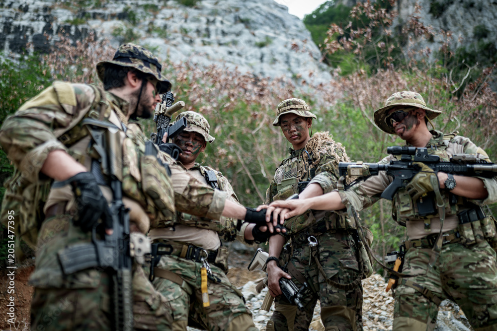 Fototapeta premium Special forces soldiers in camouflage gear huddle together in a rocky, wooded area