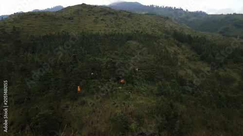 4K drone shot of a hidden orange camping tent inside a lush green mountain forest.
