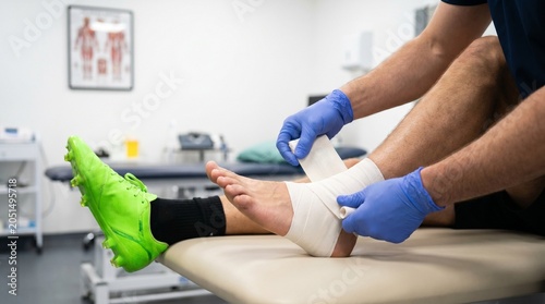 Physiotherapist wraps injured ankle of athlete in clinic for medical treatment