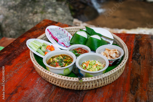 Traditional Northern Thai food set served in a rattan Khantoke tray on a wooden table.