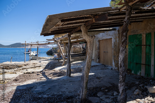 «Ibiza, Spain»; May 26 2026: Sa Caleta traditional fisherman huts and rustic wooden docks in a narrow rocky bay, showcasing the historic coastal heritage and turquoise Mediterranean sea.